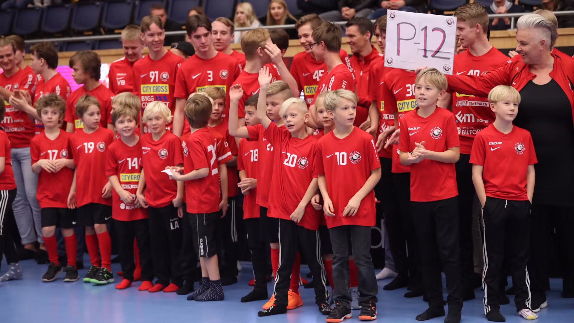 Ungdomar i röda tröjor och ledare samlade för ett lagfoto i arenan