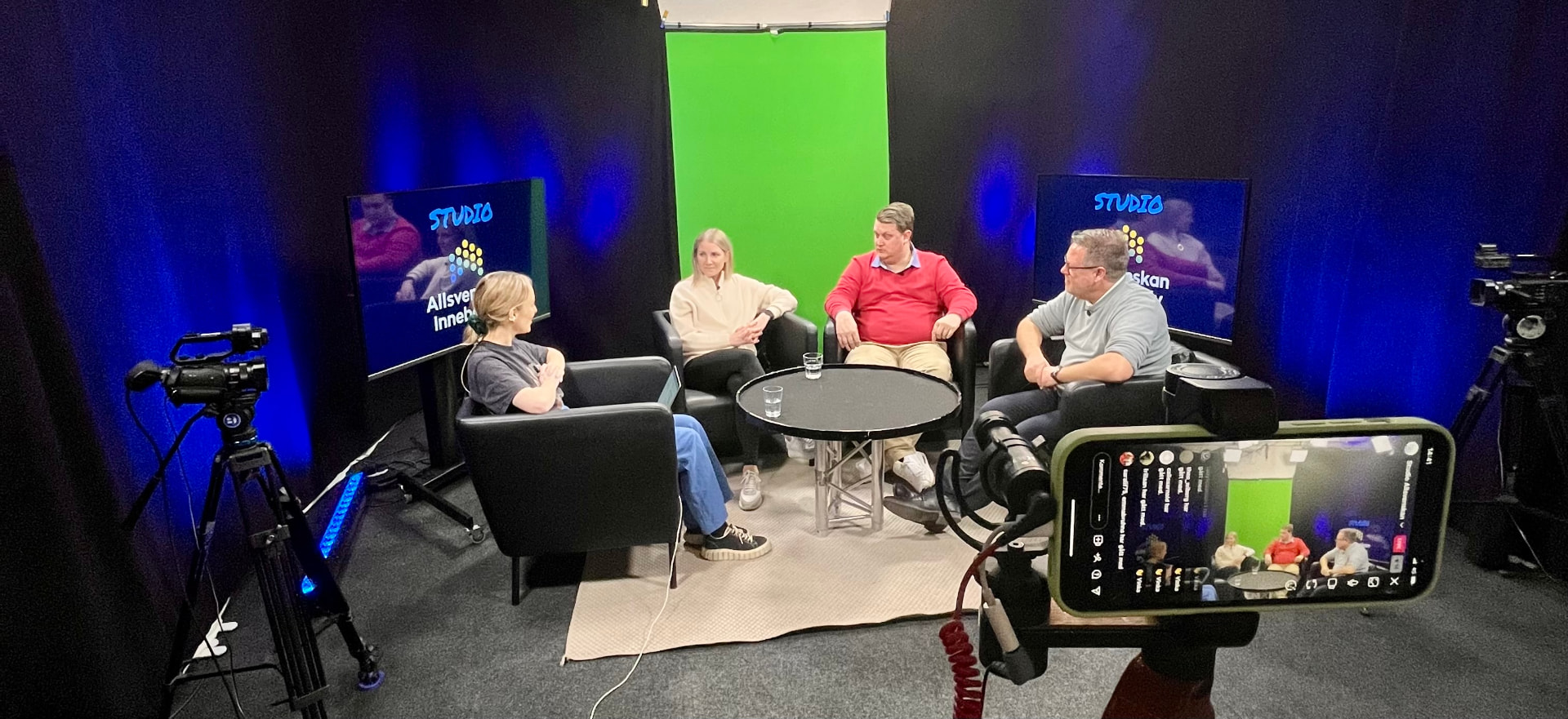 Sändningsplats i en studio med fyra personer, kameror och en telefon som visar en pågående livesändning